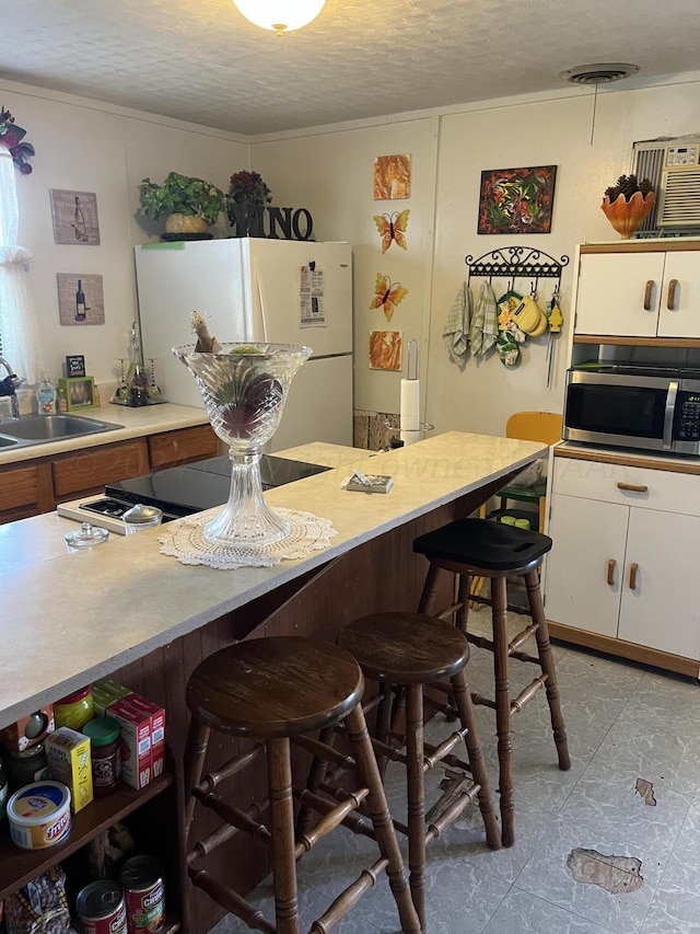 kitchen with white fridge, white cabinetry, a textured ceiling, sink, and a breakfast bar