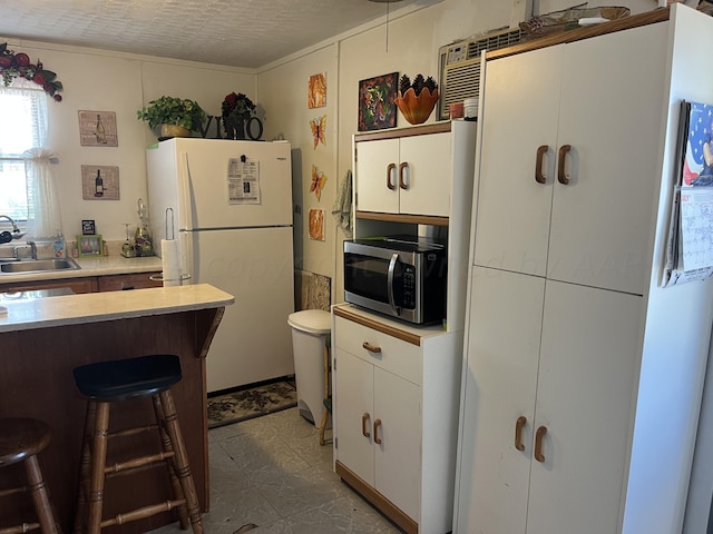 kitchen with white refrigerator, white cabinets, a textured ceiling, sink, and a breakfast bar