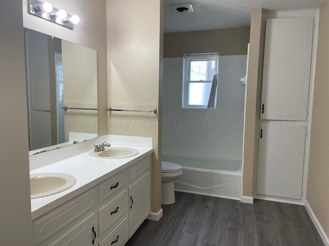 full bathroom featuring hardwood / wood-style floors, vanity,  shower combination, toilet, and a textured ceiling