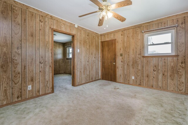 spare room featuring wood walls, ceiling fan, and light colored carpet