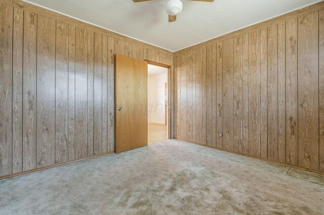 spare room with ceiling fan, wooden walls, and light carpet