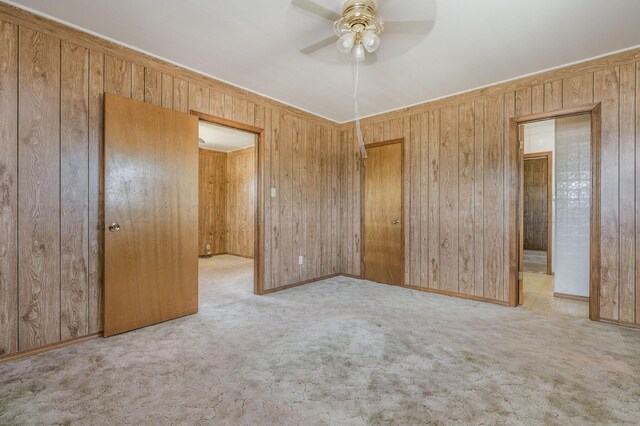 unfurnished bedroom featuring ceiling fan, wooden walls, light carpet, and a closet