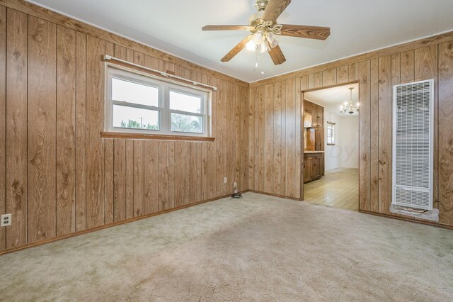 carpeted empty room featuring wood walls and ceiling fan with notable chandelier