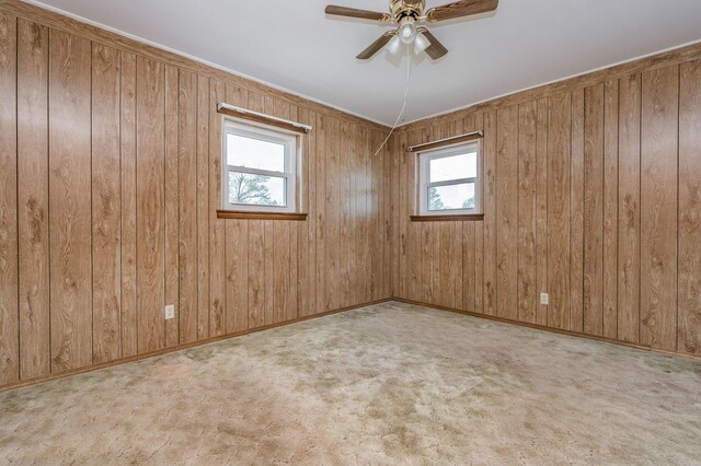 unfurnished room featuring a wealth of natural light, ceiling fan, wooden walls, and light carpet