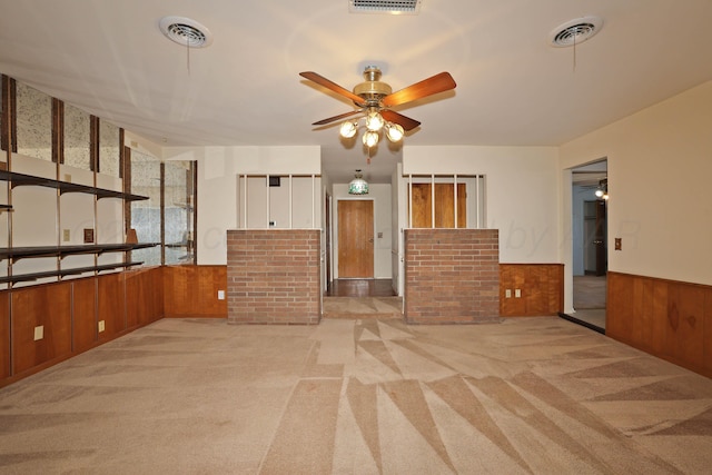 carpeted spare room featuring wainscoting, wood walls, and a ceiling fan