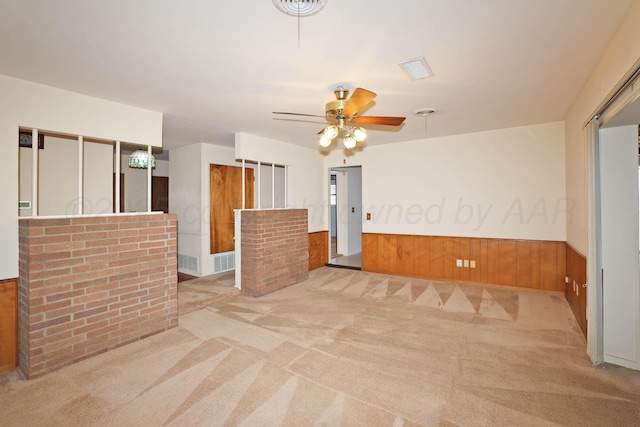 carpeted empty room featuring wooden walls, a wainscoted wall, and ceiling fan