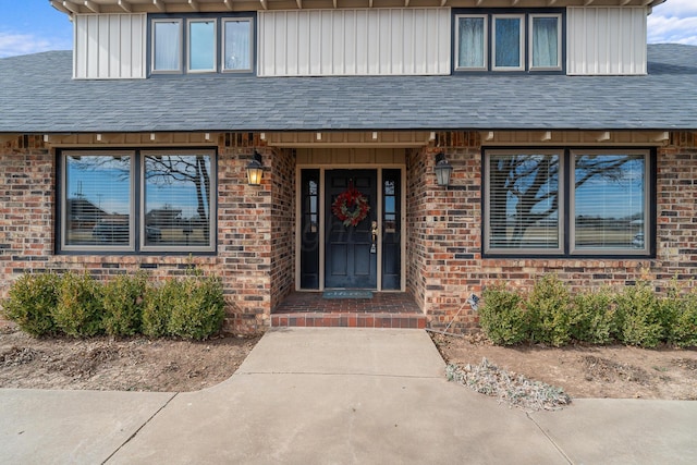 view of exterior entry featuring brick siding and roof with shingles