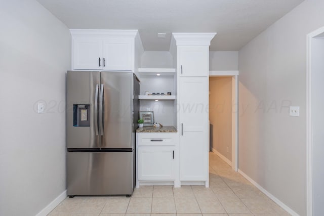 kitchen with dark stone countertops, light tile patterned flooring, stainless steel fridge, baseboards, and white cabinetry