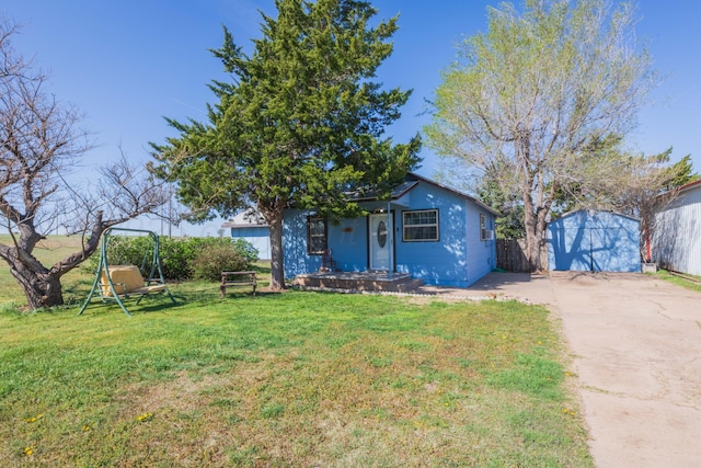 bungalow-style home with concrete driveway, a front yard, an outdoor structure, and fence