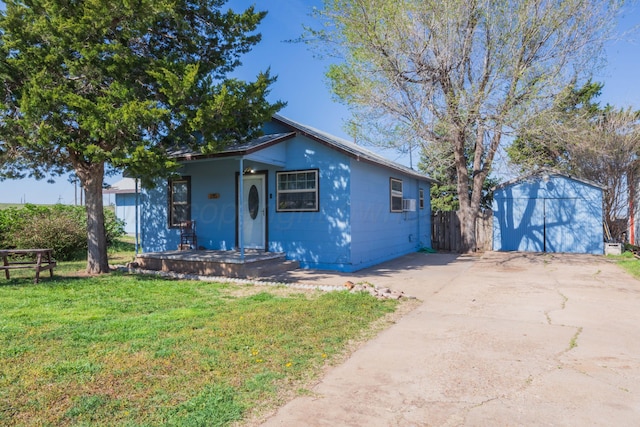 bungalow-style house featuring an outdoor structure, driveway, a front yard, concrete block siding, and covered porch