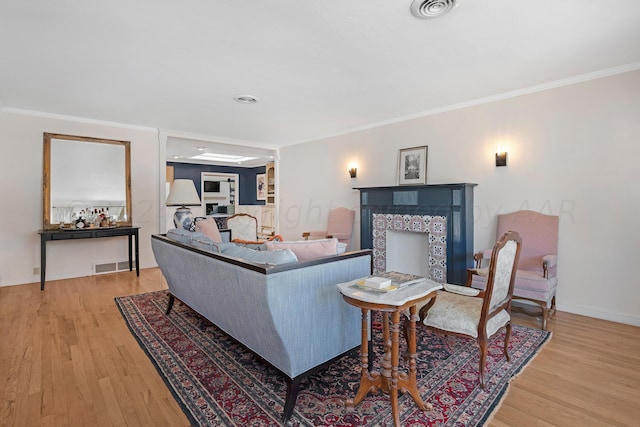 living area with wood finished floors, crown molding, baseboards, and a tiled fireplace