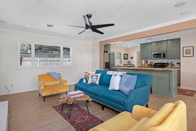 living area featuring light wood finished floors, baseboards, ceiling fan, crown molding, and recessed lighting