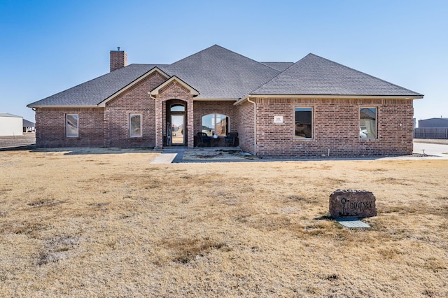 view of front of home featuring a shingled roof, brick siding, a chimney, and a front lawn