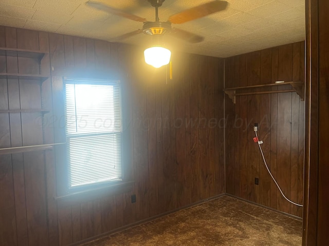 empty room with wooden walls, dark carpet, and a ceiling fan