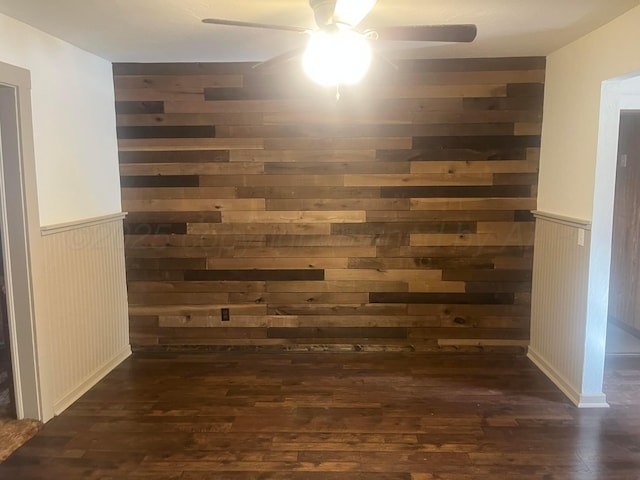 interior details featuring wainscoting, wood finished floors, a ceiling fan, and wooden walls