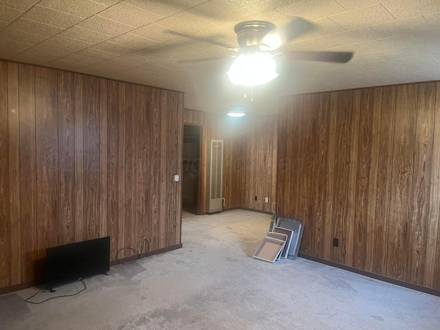 carpeted spare room with wood walls and ceiling fan