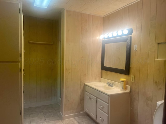 bathroom with a stall shower, baseboards, tile patterned flooring, vanity, and wood walls