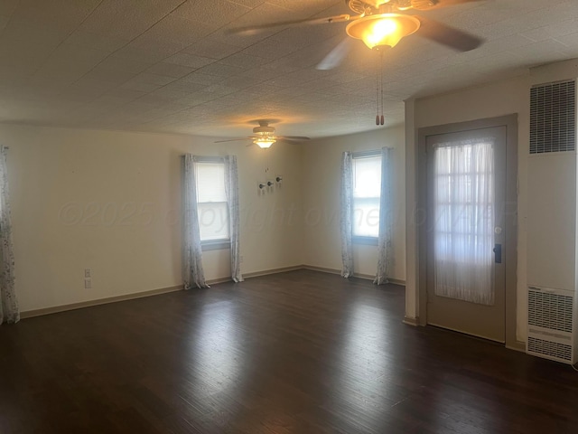 empty room featuring dark wood-style floors, ceiling fan, a heating unit, and baseboards