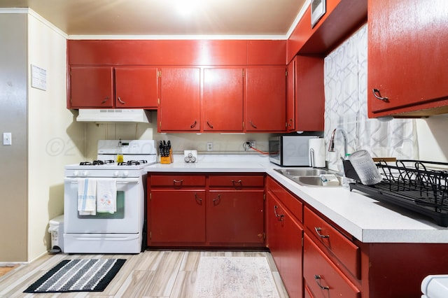 kitchen featuring a sink, light countertops, under cabinet range hood, white gas range, and red cabinets