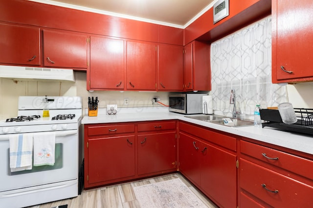 kitchen featuring red cabinets, stainless steel microwave, under cabinet range hood, and white range with gas stovetop