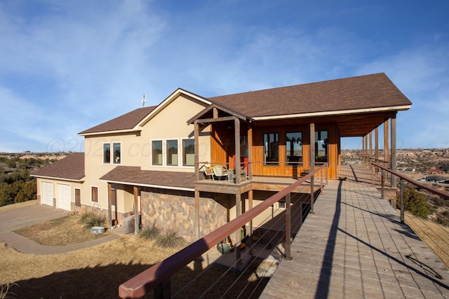 rear view of property with roof with shingles, stucco siding, stone siding, and concrete driveway