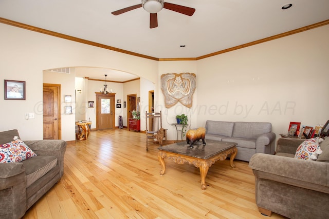 living room with ceiling fan, visible vents, arched walkways, light wood finished floors, and ornamental molding