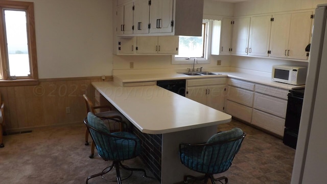 kitchen with black dishwasher, kitchen peninsula, wood walls, sink, and a kitchen breakfast bar