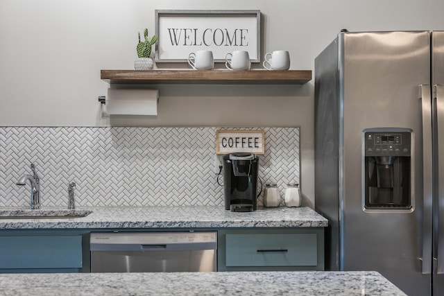 kitchen with appliances with stainless steel finishes, sink, backsplash, and light stone countertops