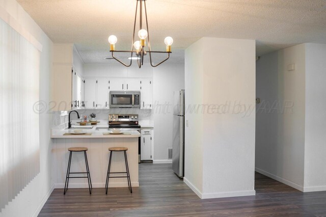 kitchen with stainless steel appliances, a peninsula, a sink, white cabinetry, and dark wood-style floors