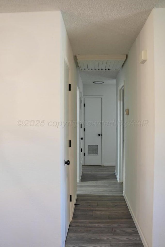 corridor with visible vents, baseboards, dark wood finished floors, and a textured ceiling