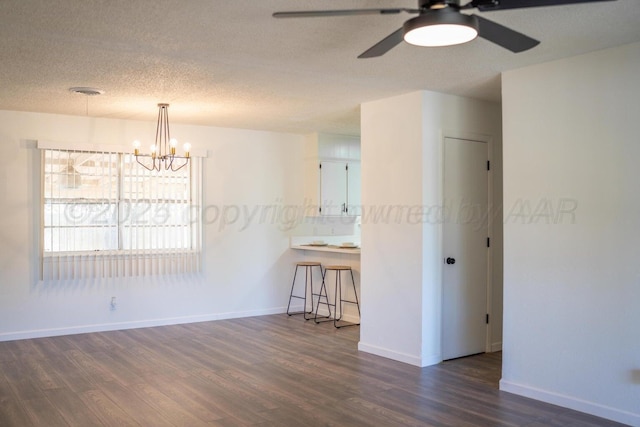 unfurnished room with a textured ceiling, dark wood-type flooring, ceiling fan with notable chandelier, and baseboards