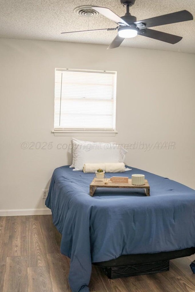 bedroom featuring a ceiling fan, visible vents, a textured ceiling, and wood finished floors