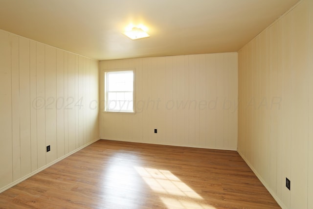 unfurnished room with wooden walls and light hardwood / wood-style floors