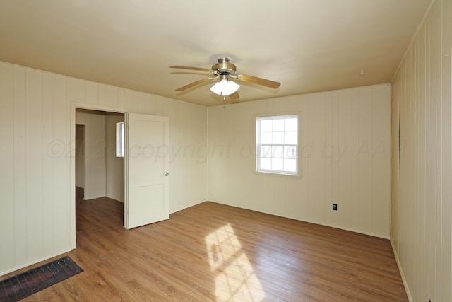 unfurnished room featuring wooden walls, hardwood / wood-style floors, and ceiling fan