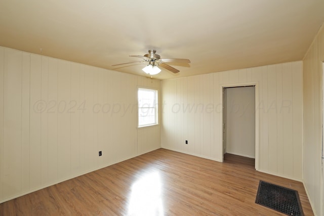 spare room featuring light wood-type flooring, ceiling fan, and wood walls