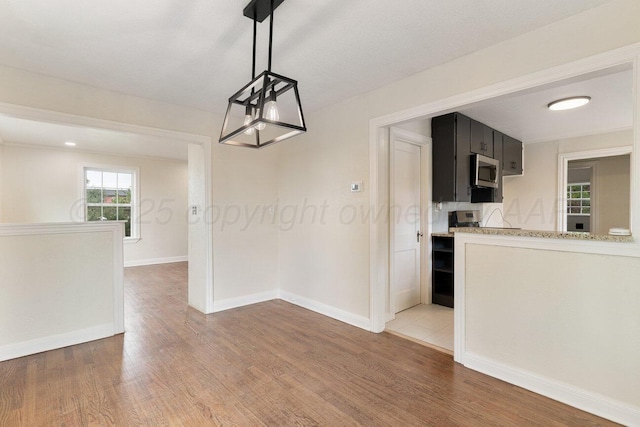 3201 S Grand St, Amarillo, TX 79103 - kitchen with stainless steel microwave, dark cabinetry, light wood-type flooring, hanging light fixtures, and light stone countertops