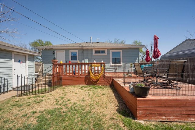 rear view of house featuring outdoor dining space, a lawn, fence, and a deck