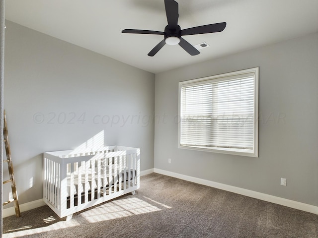 carpeted bedroom with visible vents, baseboards, a nursery area, and ceiling fan