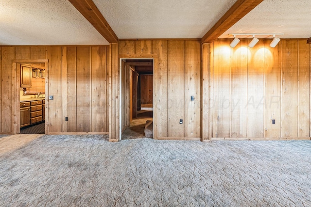 unfurnished room with carpet flooring, beam ceiling, and a textured ceiling