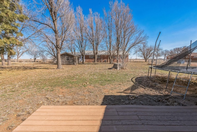 view of yard featuring a trampoline, a storage shed, a rural view, and a wooden deck