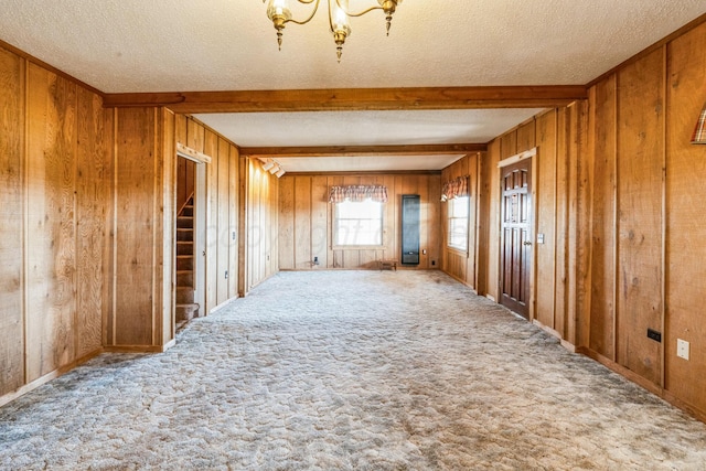 spare room featuring beam ceiling, light colored carpet, a textured ceiling, and wooden walls