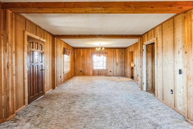 carpeted empty room featuring beamed ceiling, a chandelier, a textured ceiling, and wooden walls