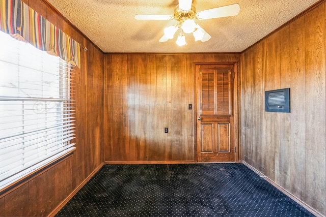 carpeted spare room featuring ceiling fan, a healthy amount of sunlight, a textured ceiling, and wood walls