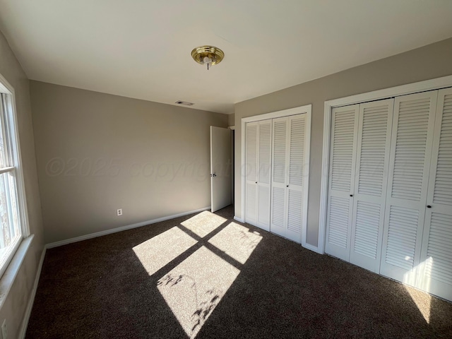 unfurnished bedroom with multiple closets and dark colored carpet