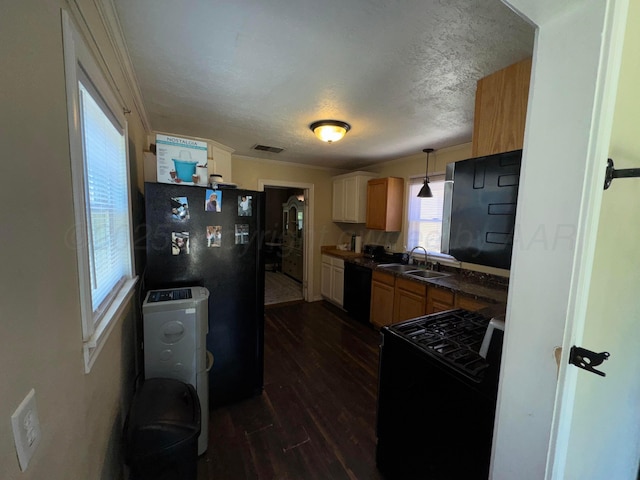 kitchen featuring black appliances, a sink, dark countertops, dark wood-style floors, and hanging light fixtures