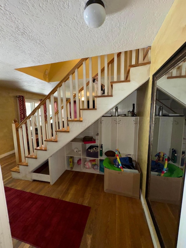 staircase featuring a textured ceiling, wood finished floors, and baseboards