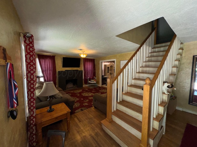 living area featuring a fireplace, stairway, a textured ceiling, and wood finished floors