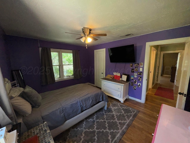 bedroom featuring baseboards, wood finished floors, a ceiling fan, a closet, and a textured ceiling