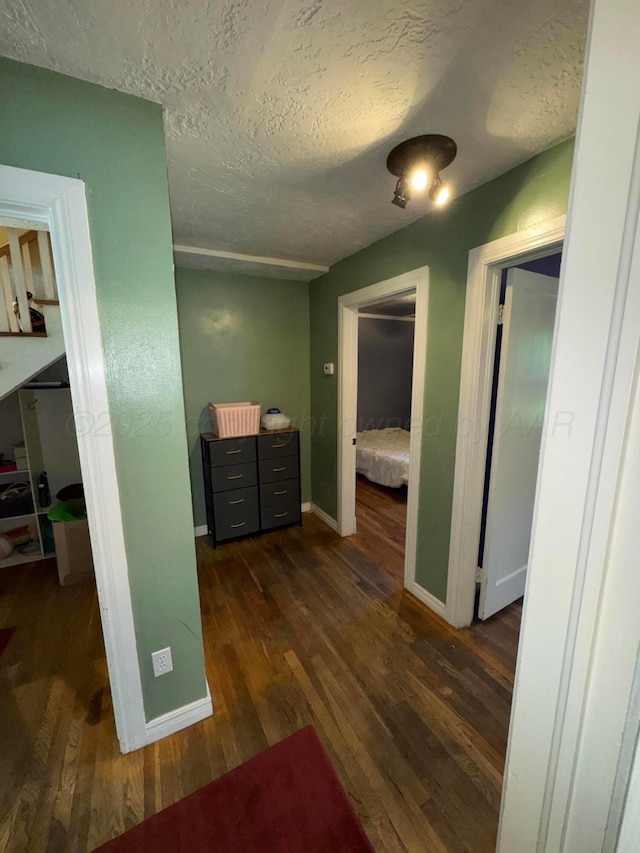 hallway with a textured ceiling, dark wood-style flooring, and baseboards