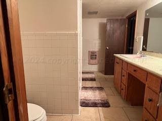 bathroom with tile walls, toilet, vanity, and tile patterned floors